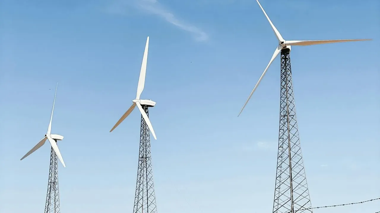 Vindkraftverk bakom ett stängsel mot blå himmel